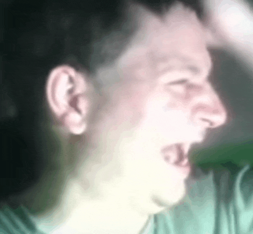 a close up of a man 's face with his mouth open and his hand behind his head .