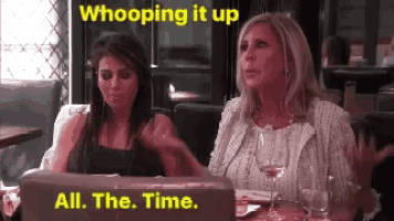 two women are sitting at a table with a laptop and a sign that says whooping it up