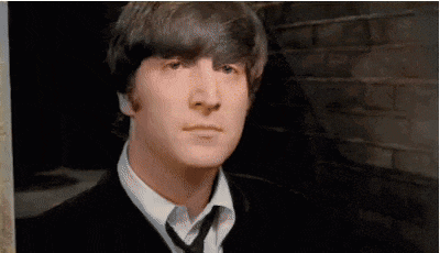john lennon is wearing a suit and tie and looking at the camera .