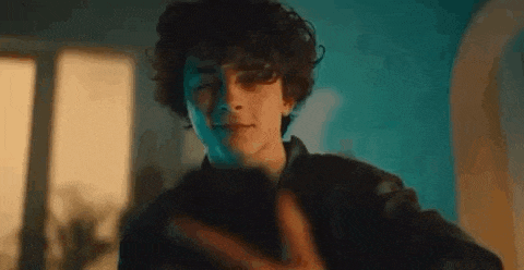 a young man with curly hair is standing in front of a window and making a funny face .