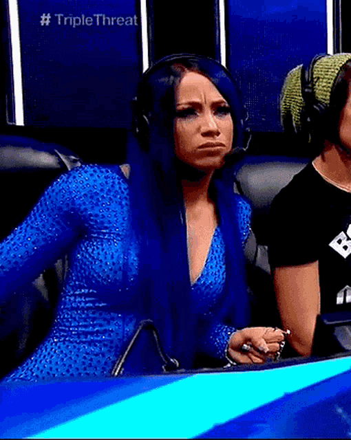 a woman with long blue hair is wearing headphones and making a face .