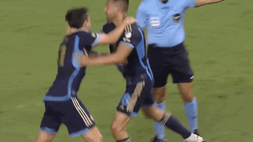 two soccer players are hugging each other on the field while a referee looks on