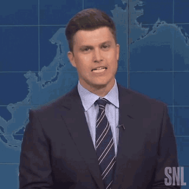 a man in a suit and tie says i think in front of a map of the world