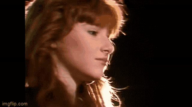 a close up of a woman 's face with red hair and a black background .