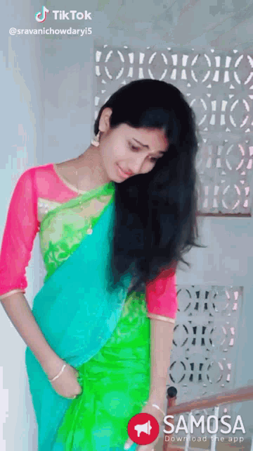 a woman in a green and blue saree is standing in front of a samosa app