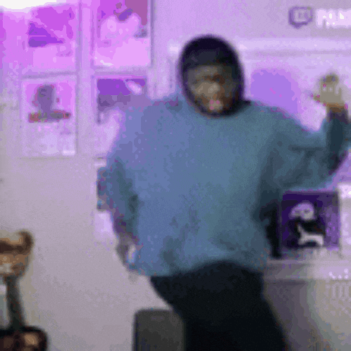 a person wearing a blue sweater and a mask is dancing in a room with purple lights .