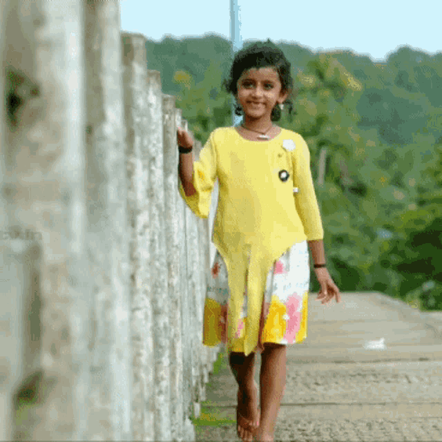 a little girl in a yellow dress is walking along a sidewalk
