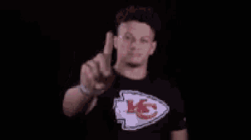 a man wearing a t-shirt with a chiefs logo is pointing up with his finger .