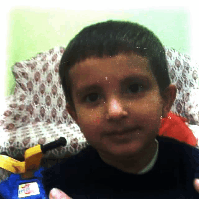 a young boy in a black shirt looks at the camera with a toy train in the background