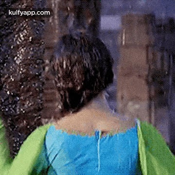 a woman in a blue top and green sleeves is standing in front of a building .