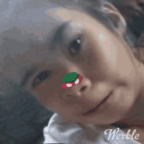a close up of a girl 's face with a sticker on her nose that looks like a ninja turtle .