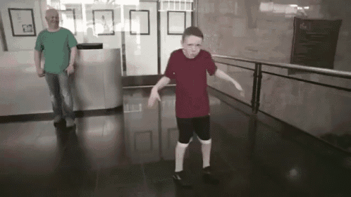 a boy in a red shirt is dancing in a hallway