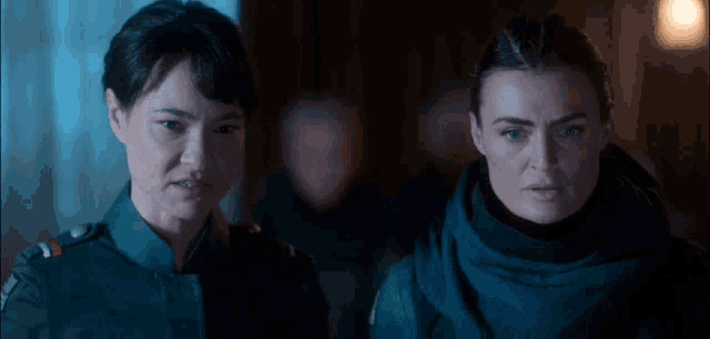 two women are standing next to each other in a dark room looking at something