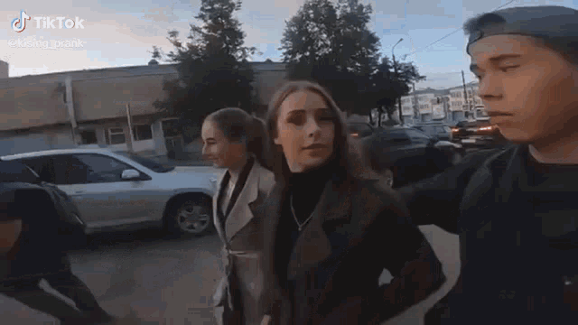 a man and two women are walking down a street in front of a white car .