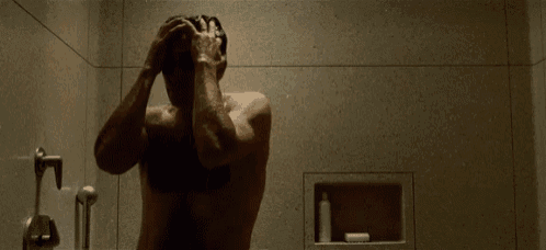 a shirtless man is taking a shower with his hands on his head