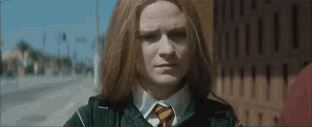 a girl with long red hair is wearing a green sweater and a red tie