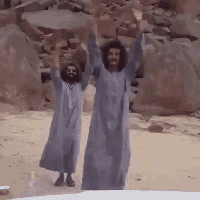 two men are standing on a beach with their hands in the air .