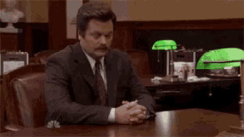 a man in a suit is sitting at a desk with his hands folded .