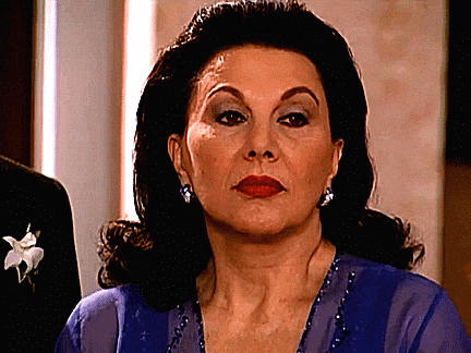 a woman in a blue dress with a flower in her hair looks at the camera