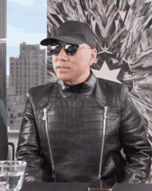a man wearing sunglasses and a leather jacket sitting at a table