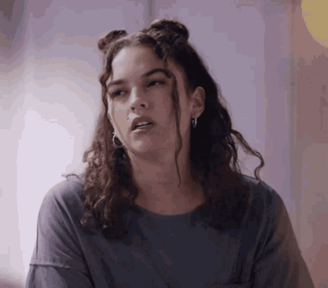 a woman with curly hair is wearing earrings and a grey shirt
