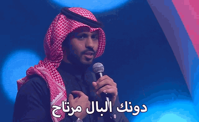 a man in a keffiyeh is holding a microphone in front of a sign in arabic