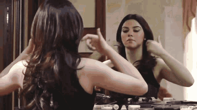 a woman in a black tank top is looking at herself in a mirror .
