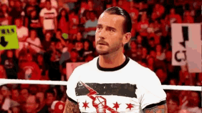 a man in a white shirt is standing in a wrestling ring in front of a crowd of people .