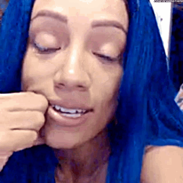 a close up of a woman with blue hair biting her nails .