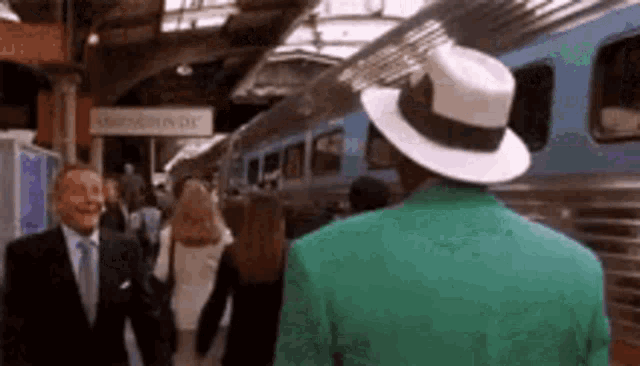 a man in a green jacket and white hat is standing next to a train .