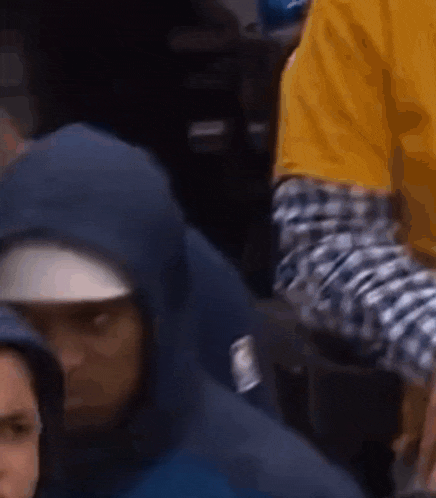 a man wearing a blue hoodie and a hat is sitting in a crowd .
