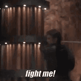 a man is standing in front of a wall with the words `` fight me '' on it .