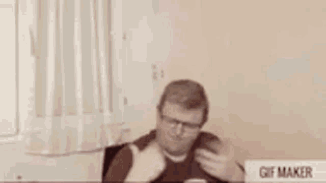 a man wearing glasses is sitting at a desk in front of a gif maker .