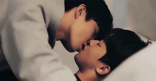 two men are kissing each other on the forehead while laying in bed .
