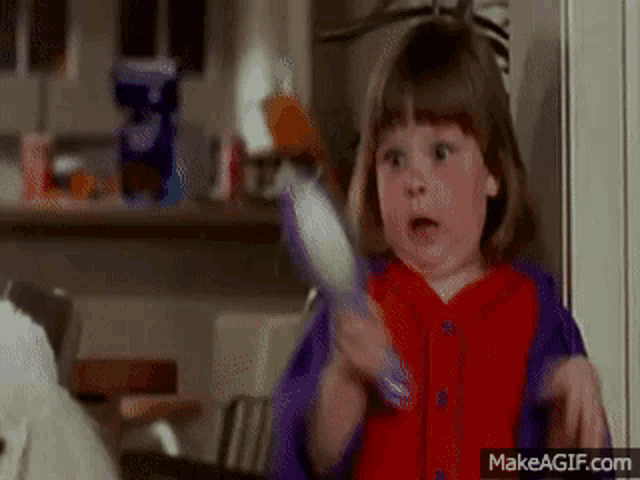 a little girl in a red and purple jacket is holding a toothbrush and making a surprised face .