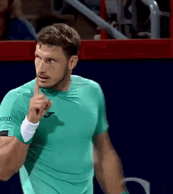 a man in a green shirt is pointing his finger up .