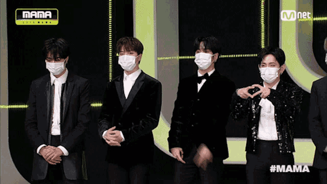 a group of men wearing face masks are standing in front of a mnet sign