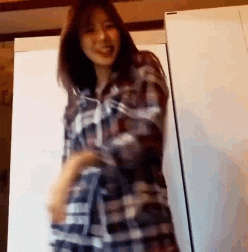 a woman in a plaid shirt is dancing in front of a refrigerator in a room .