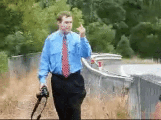 a man in a blue shirt and red tie is walking with a camera and giving the middle finger