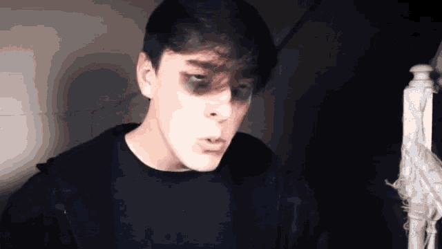 a young man with black eyes and a black shirt is standing in a dark room .