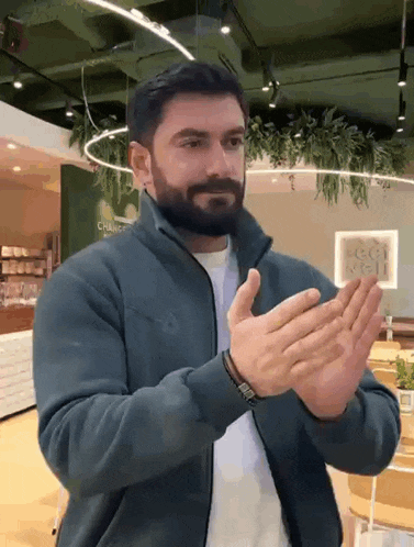 a man with a beard wearing a blue jacket is clapping his hands