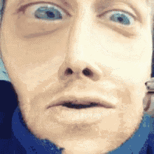 a close up of a man 's face with blue eyes and a surprised look on his face