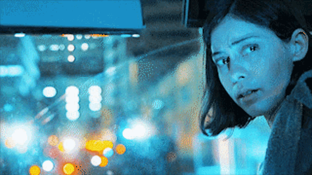 a woman is looking out a window with a blurry background and a sign that says ' a ' on it