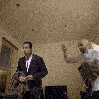 a man in a suit is standing next to a man in a white shirt in a living room .