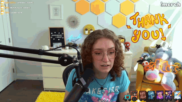 a woman in a blue shirt stands in front of a microphone with a thank you message behind her