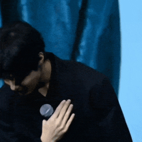 a man in a black jacket is holding a microphone to his chest .