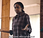 a woman in a brown shirt is standing in front of a window and talking to someone