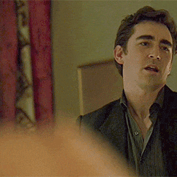 a man in a suit and shirt is standing in a room and looking at something .