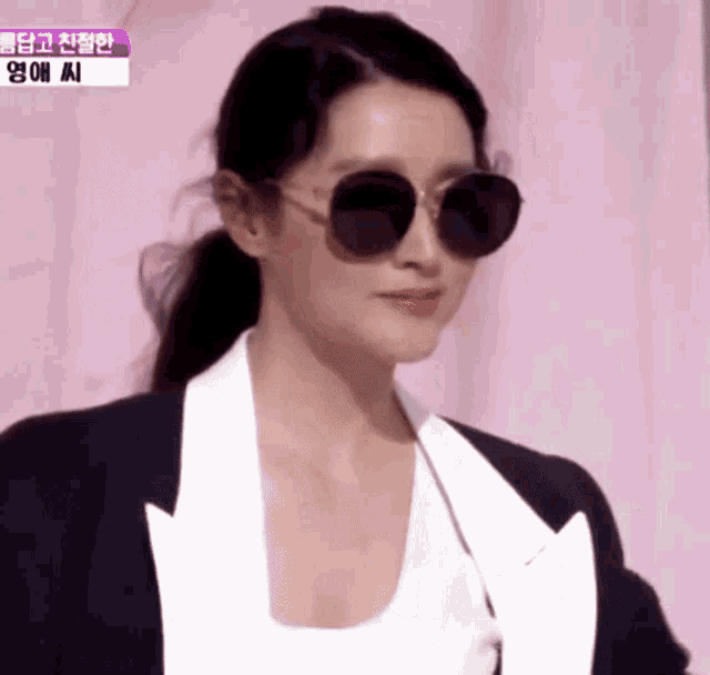 a woman wearing sunglasses and a white shirt is standing in front of a sign that says ' yy ' on it