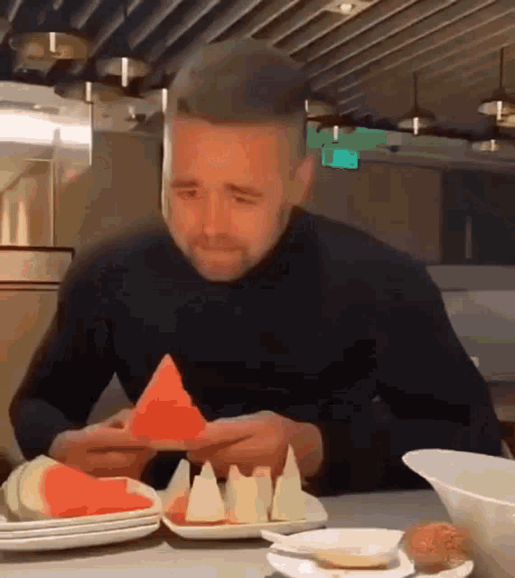 a man in a black turtleneck is eating a slice of watermelon